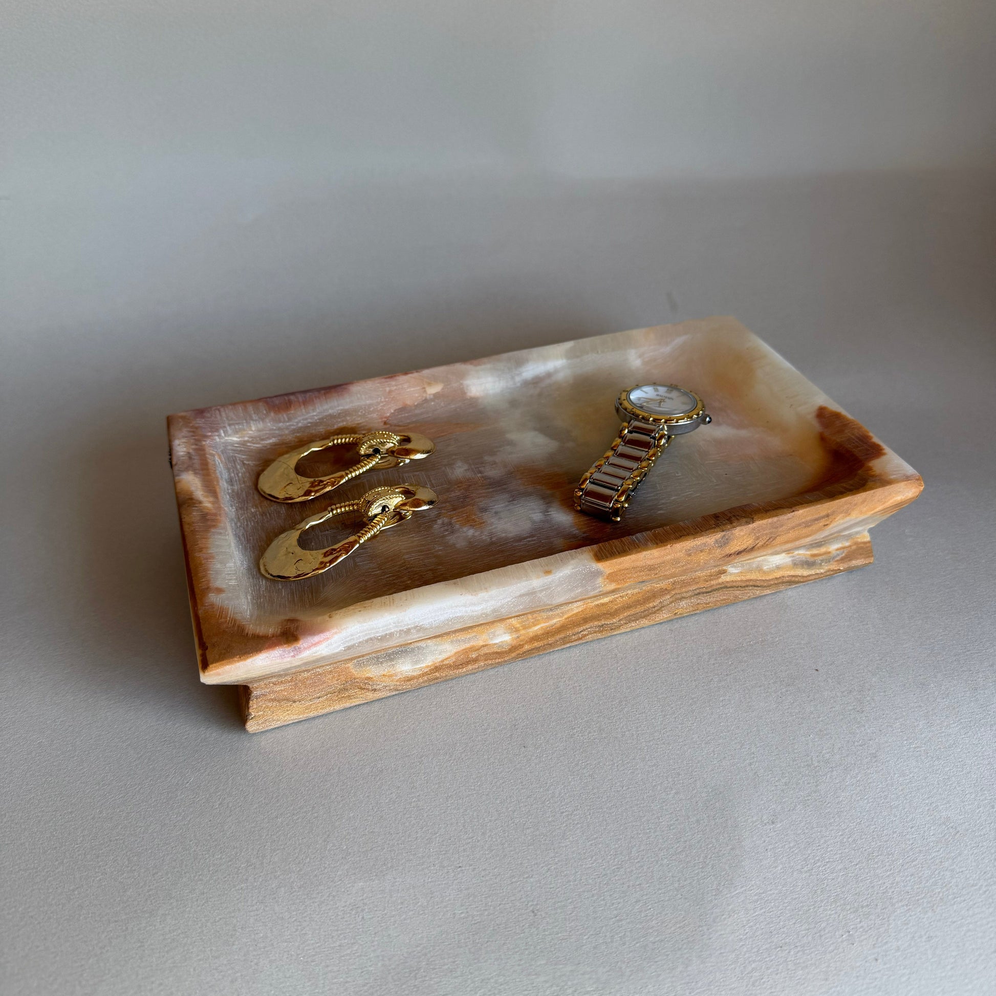 Rectangular stone jewelry dish with gold earrings on a light gray background