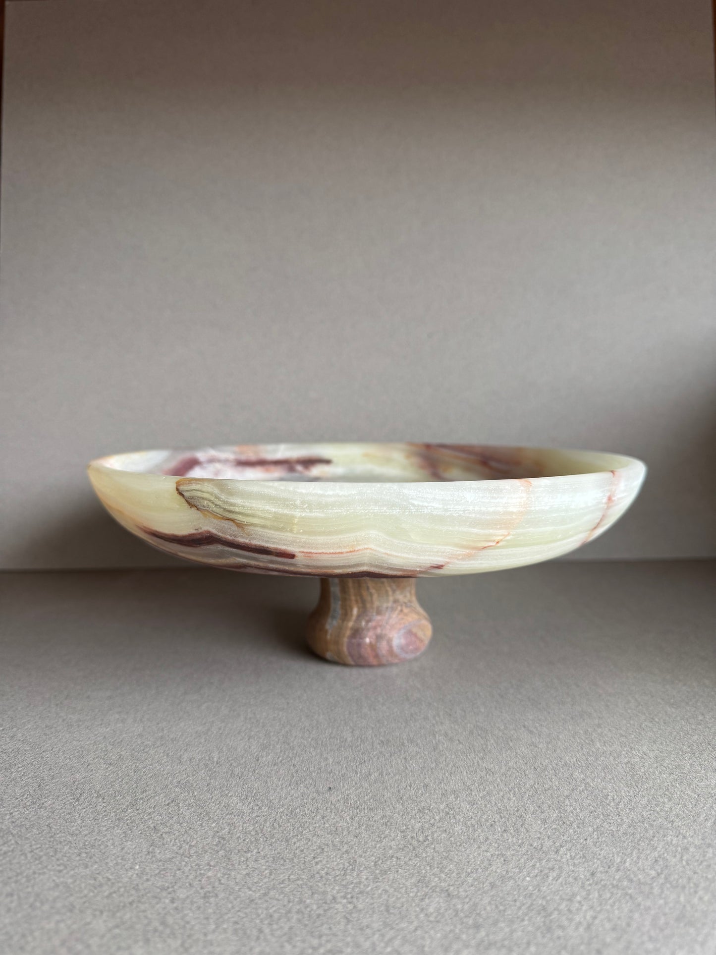 Hand-carved onyx pedestal bowl with cream, rust, and amber veining, displayed on a neutral tabletop