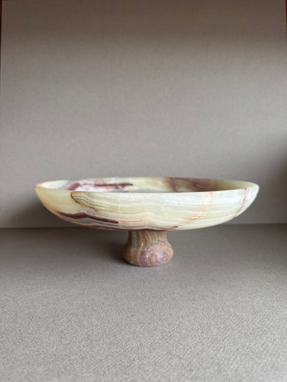 Hand-carved onyx pedestal bowl with cream, rust, and amber veining, displayed on a neutral tabletop