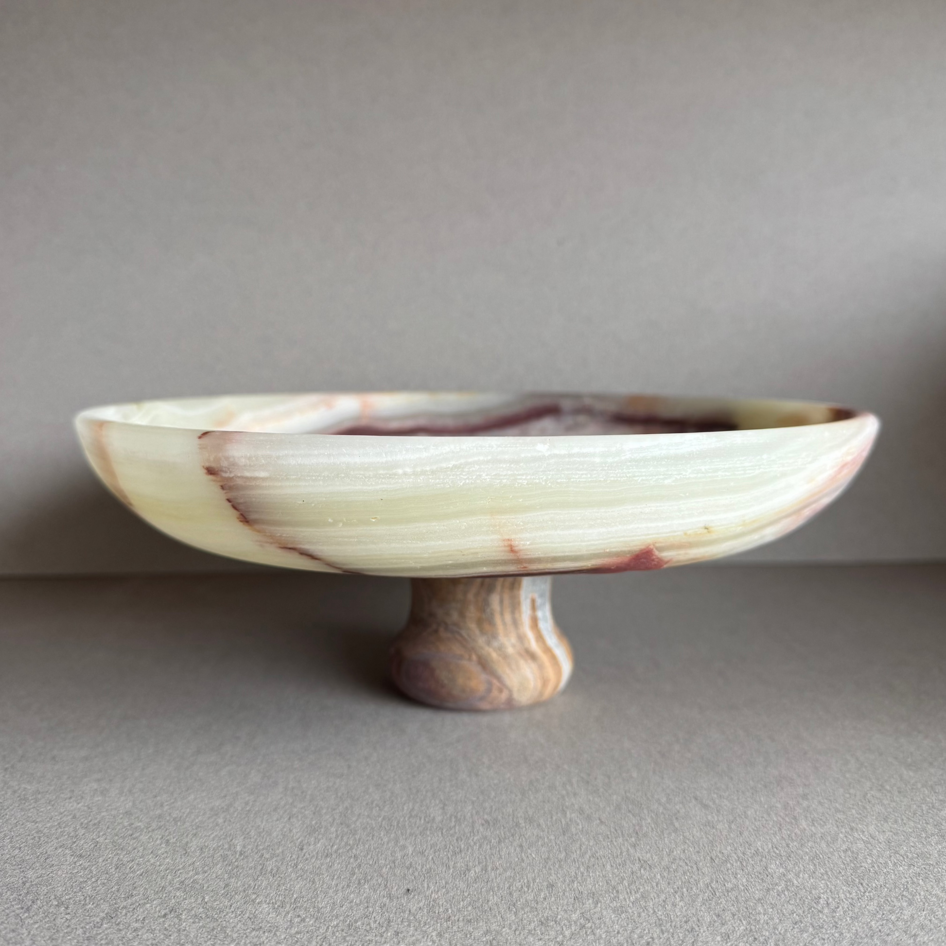 Hand-carved onyx pedestal bowl with cream, rust, and amber veining, displayed on a neutral tabletop