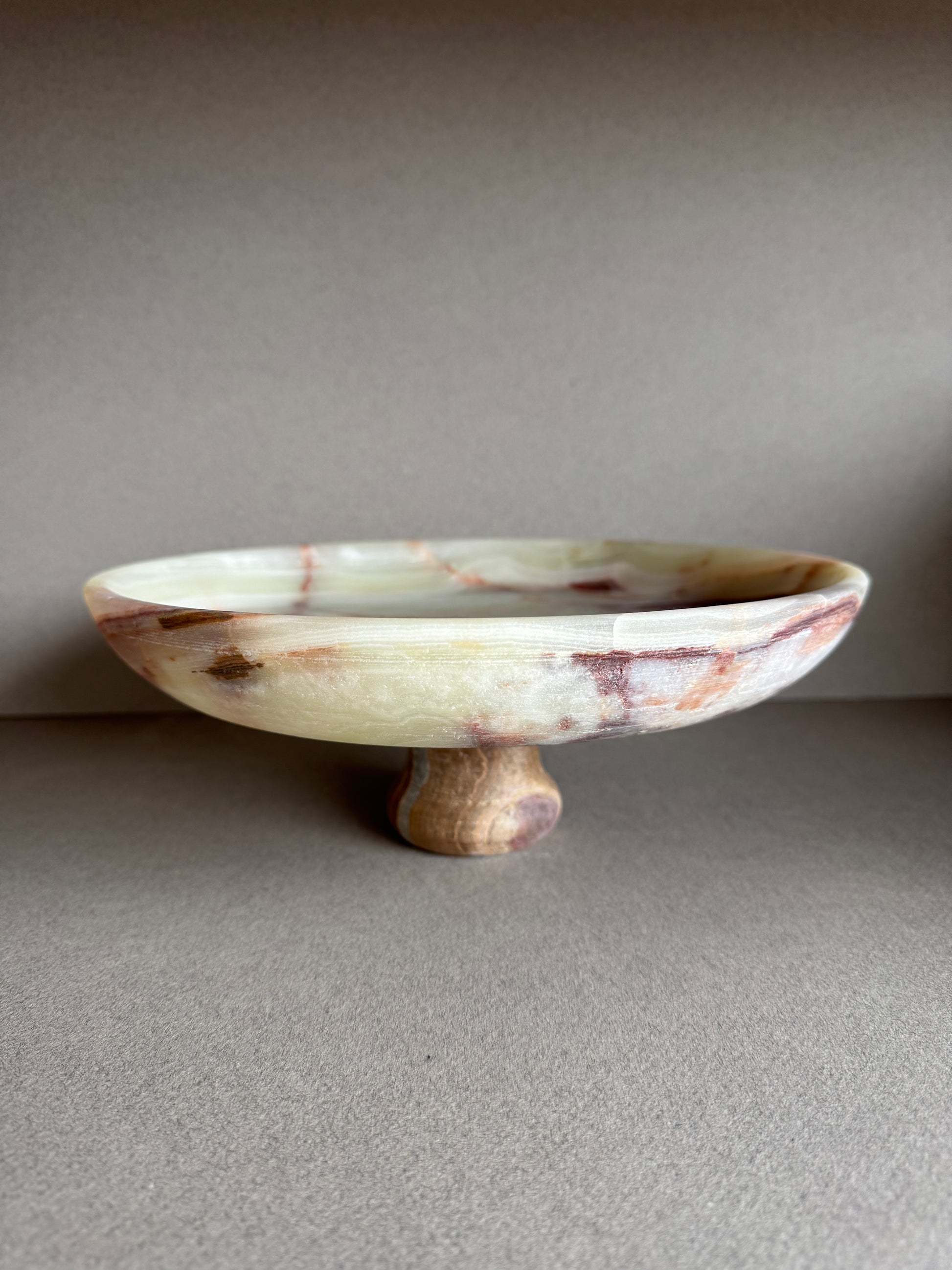 Hand-carved onyx pedestal bowl with cream, rust, and amber veining, displayed on a neutral tabletop

