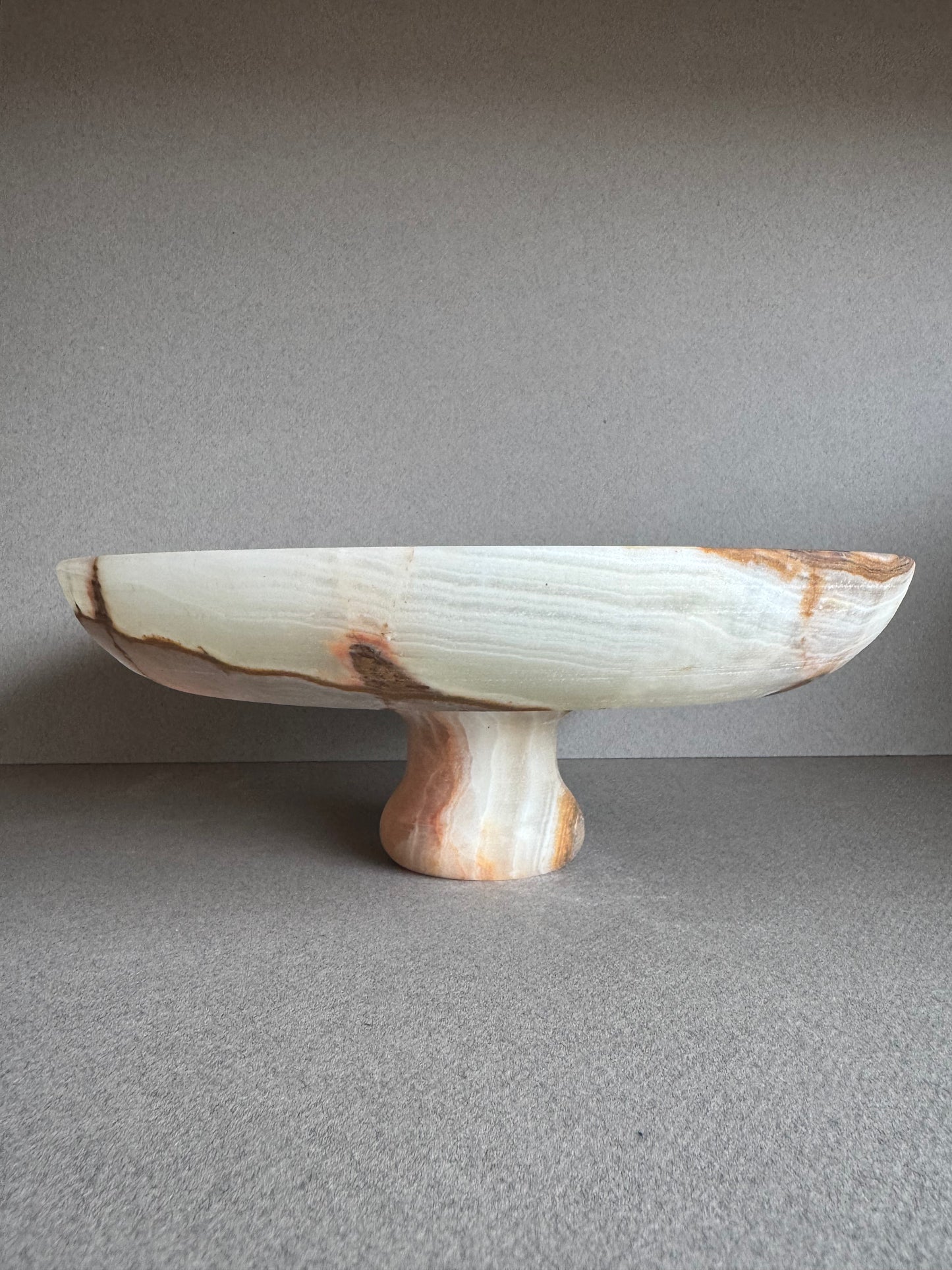 Overhead view of sculptural onyx bowl showcasing natural green and amber veining in a smooth stone surface

