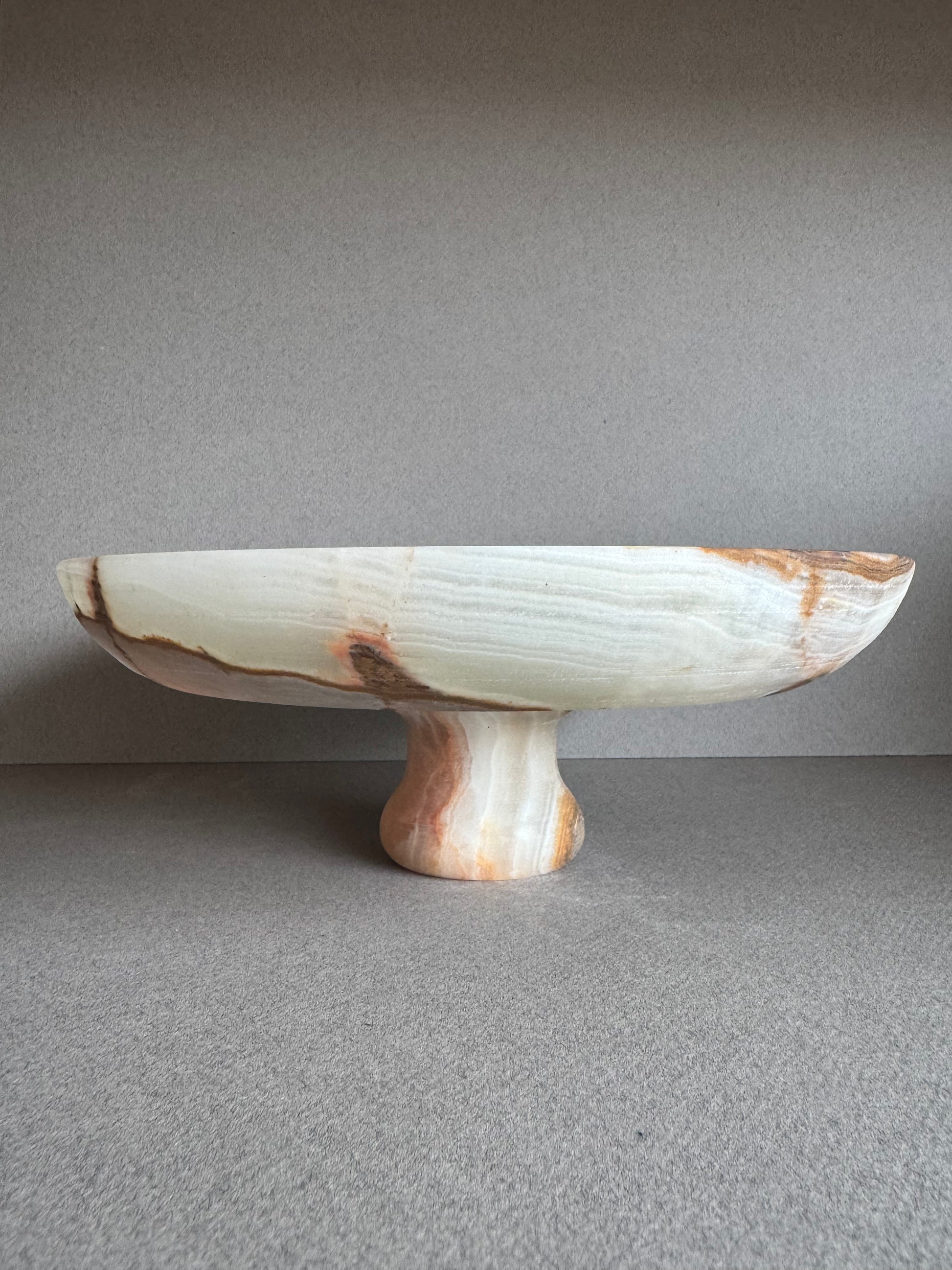 Overhead view of sculptural onyx bowl showcasing natural green and amber veining in a smooth stone surface

