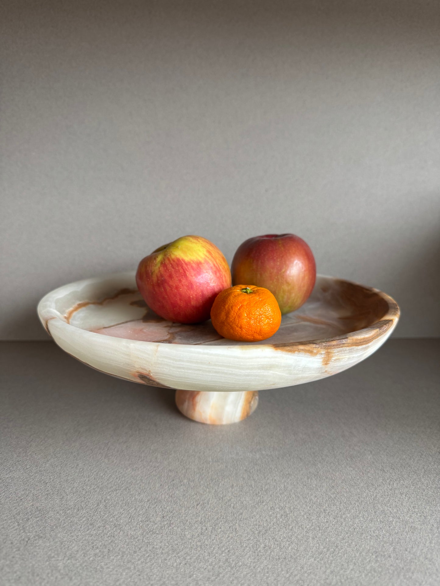Close-up of onyx bowl used as a fruit bowl showing detailed marbling in soft olive and cream tones

