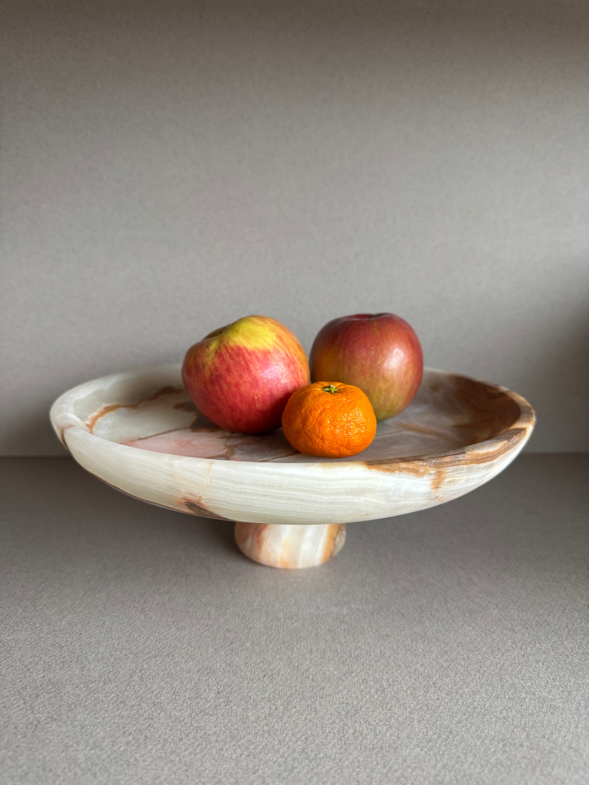 Close-up of onyx bowl used as a fruit bowl showing detailed marbling in soft olive and cream tones

