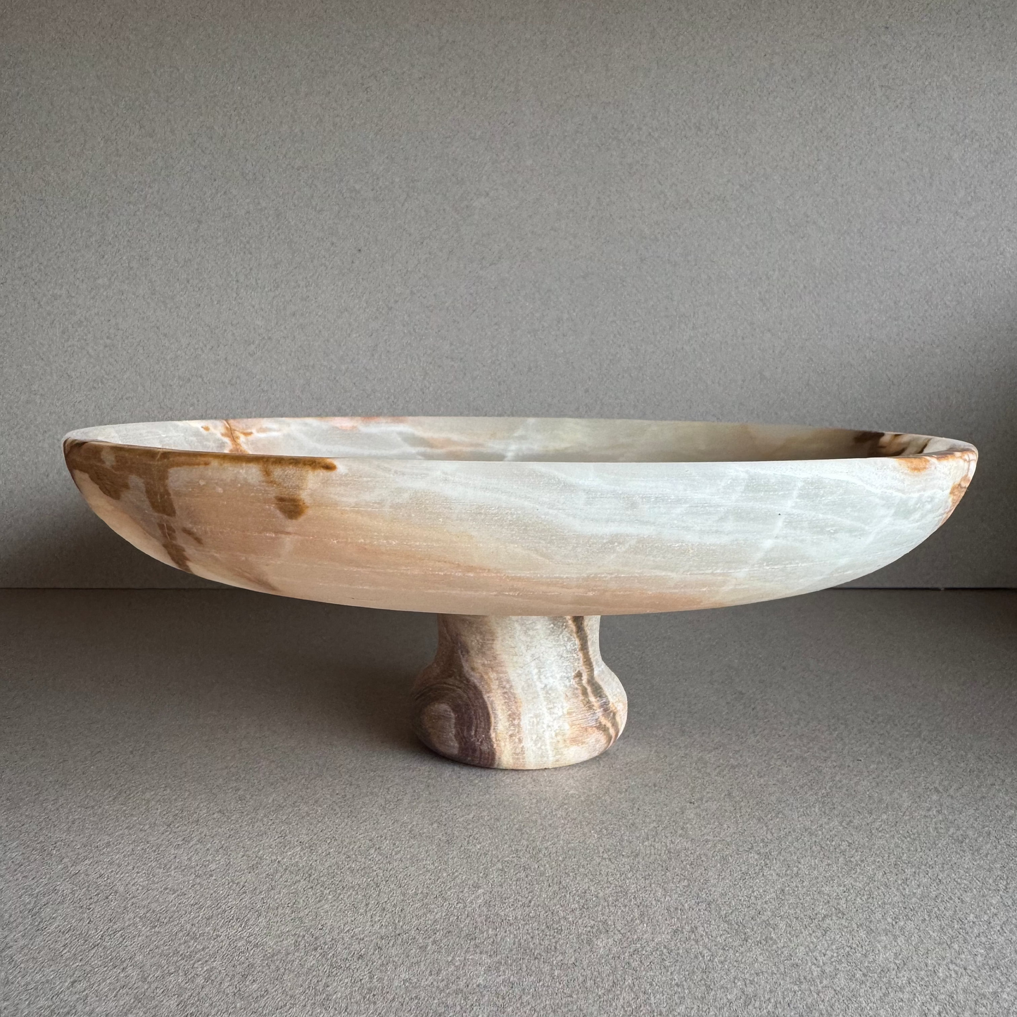 Ash, sage, and ivory onyx pedestal bowl displayed on a minimal surface, showing soft natural veining
