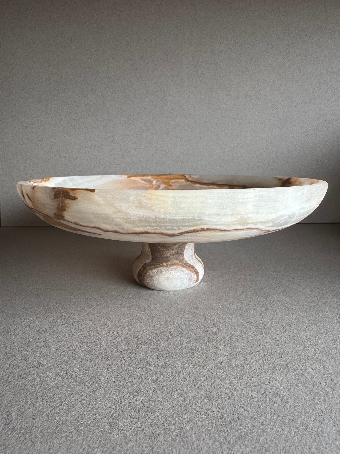 Onyx pedestal bowl styled with natural light, emphasizing its muted green and stone tones
