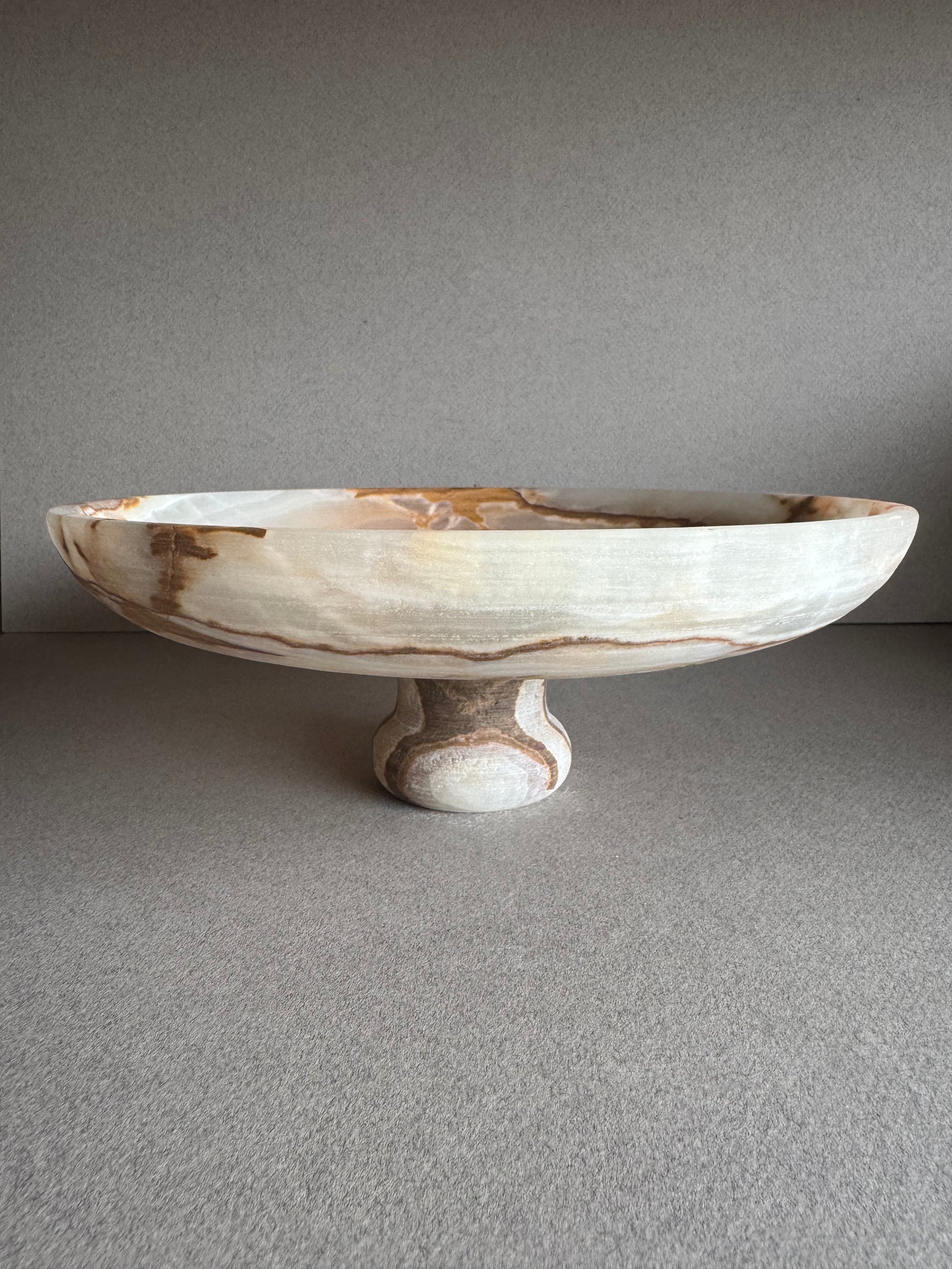 Onyx pedestal bowl styled with natural light, emphasizing its muted green and stone tones