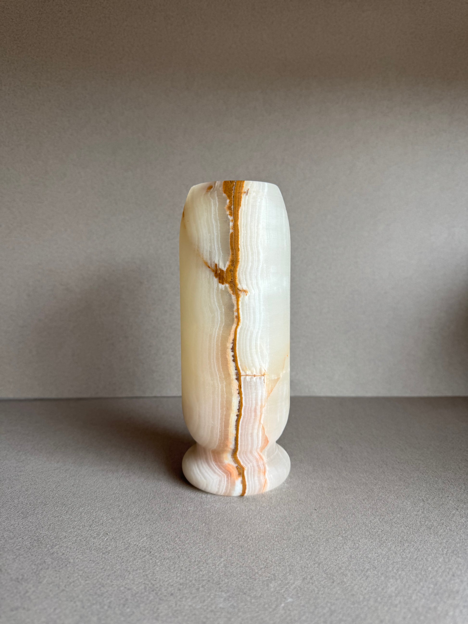 Front view of natural stone vase with warm cream body and rust-colored banding.

