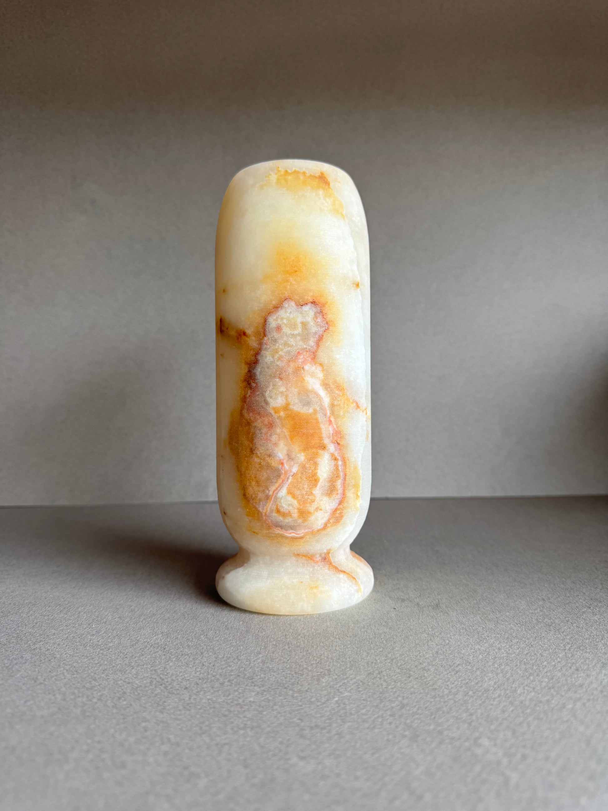 Rear floral-styled view of vase with soft golden-pink stone gradient and pedestal base.

