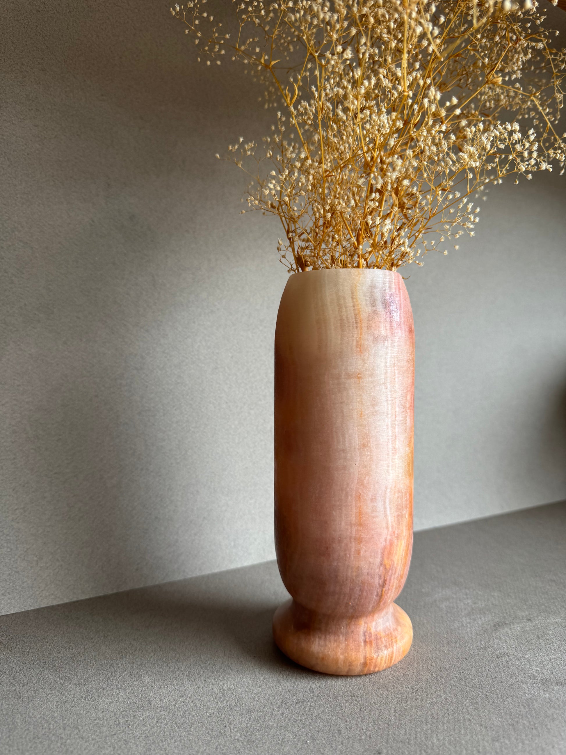 Vase styled with dried baby’s breath, highlighting warm pink and clay-like tones.

