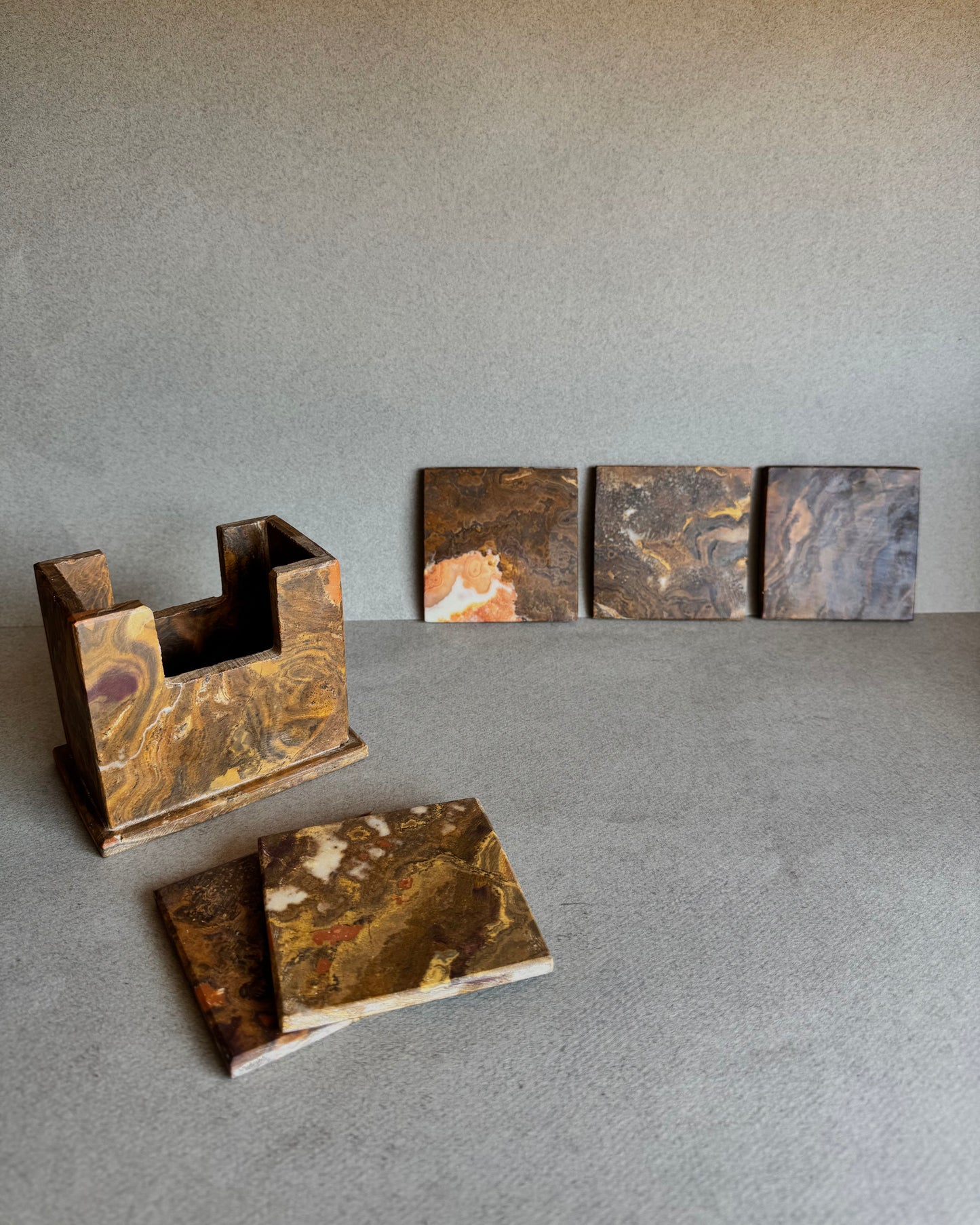 Onyx coaster set in rust, ochre, and maroon tones with holder and coasters displayed in front

