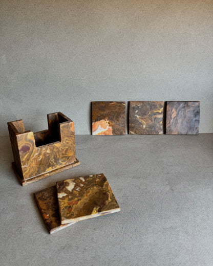 Onyx coaster set in rust, ochre, and maroon tones with holder and coasters displayed in front

