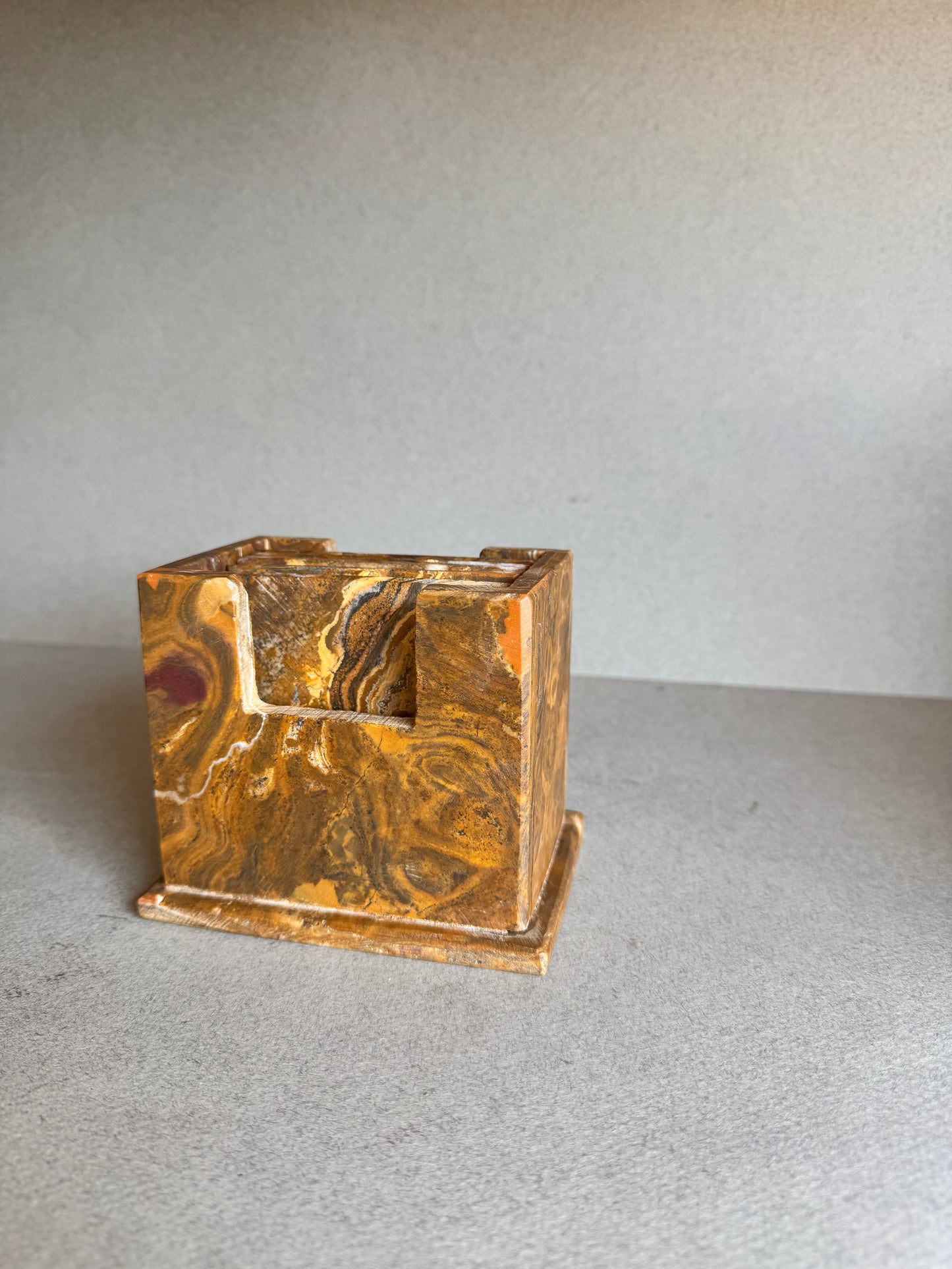 Side angle of sculptural onyx coaster holder in layered rust and brown stone patterns

