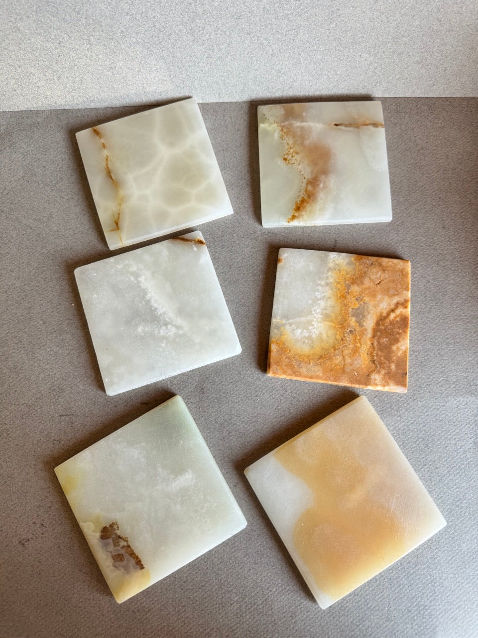 Flat lay of six square onyx coasters showing unique amber, honey, and cream veining

