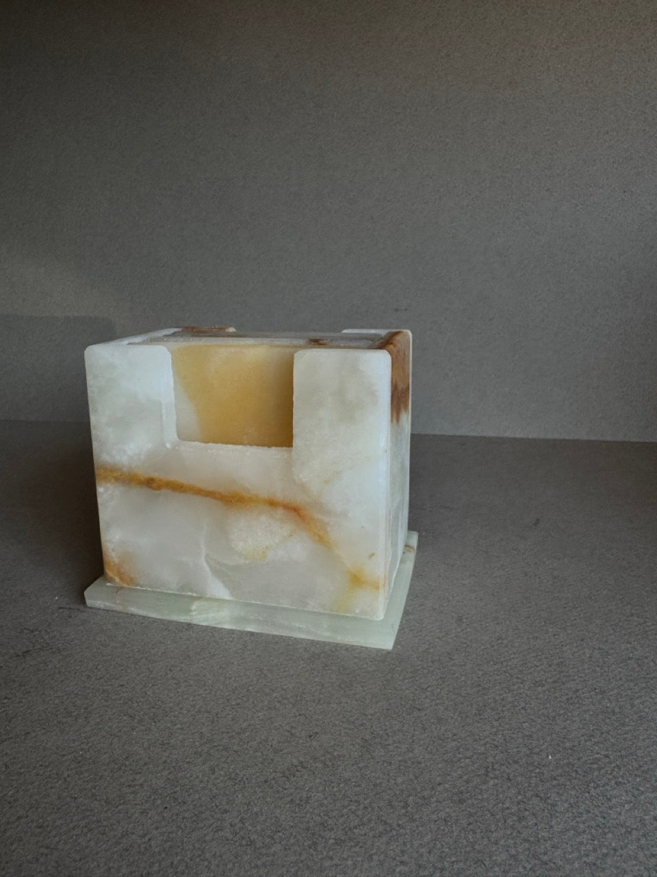 Side view of onyx coaster set in cream, amber, and honey tones inside matching carved holder

