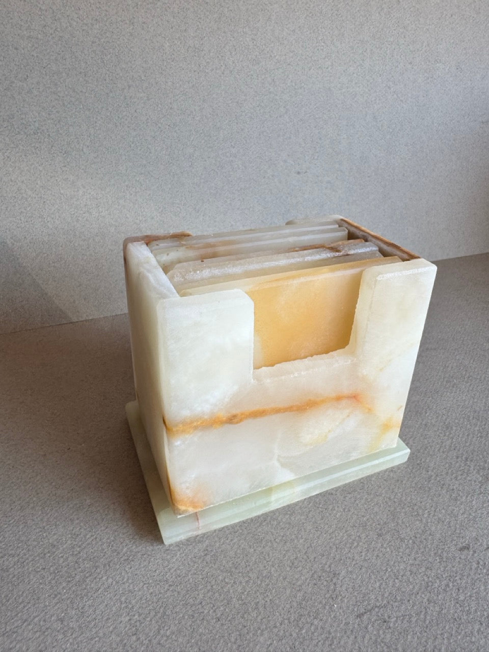 Side view of onyx coaster set in cream, amber, and honey tones inside matching carved holder

