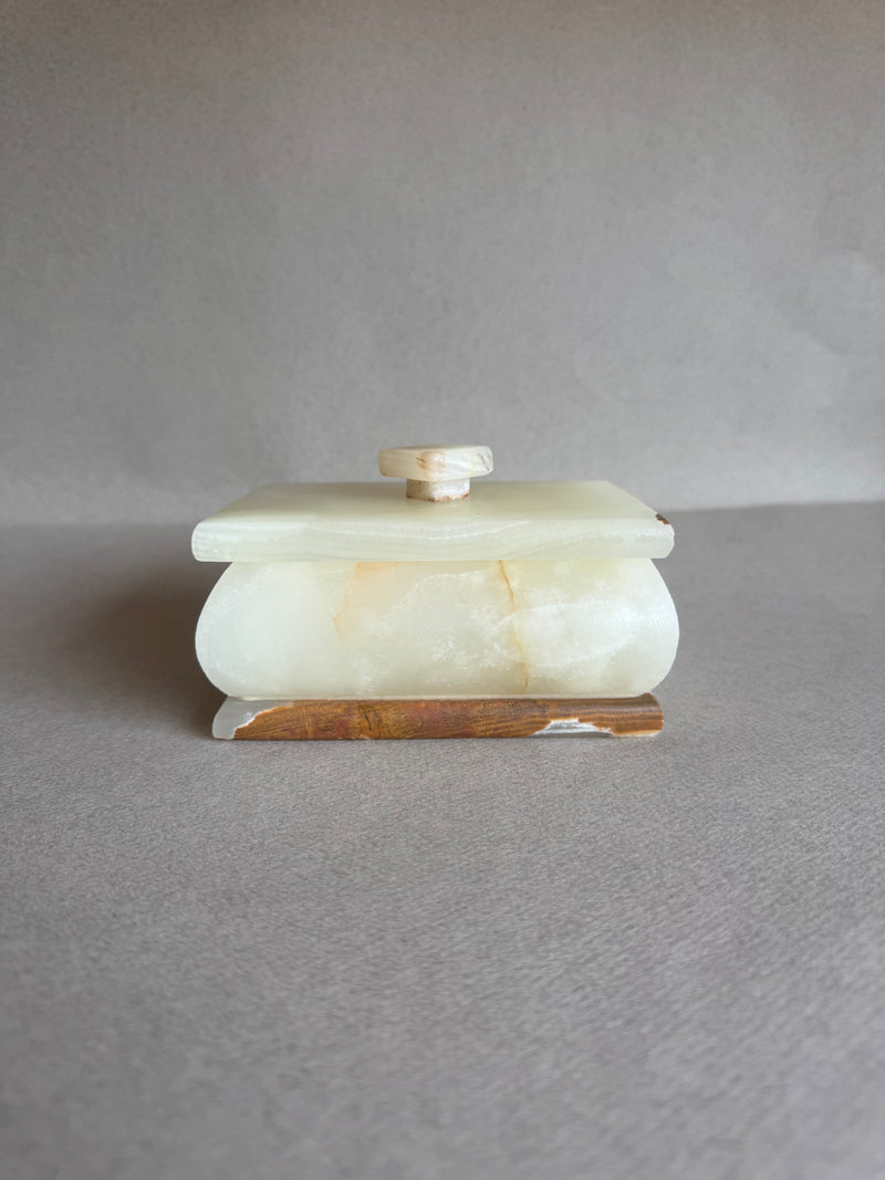 Hand-carved stone box with sculptural pull lid, resting on neutral surface


