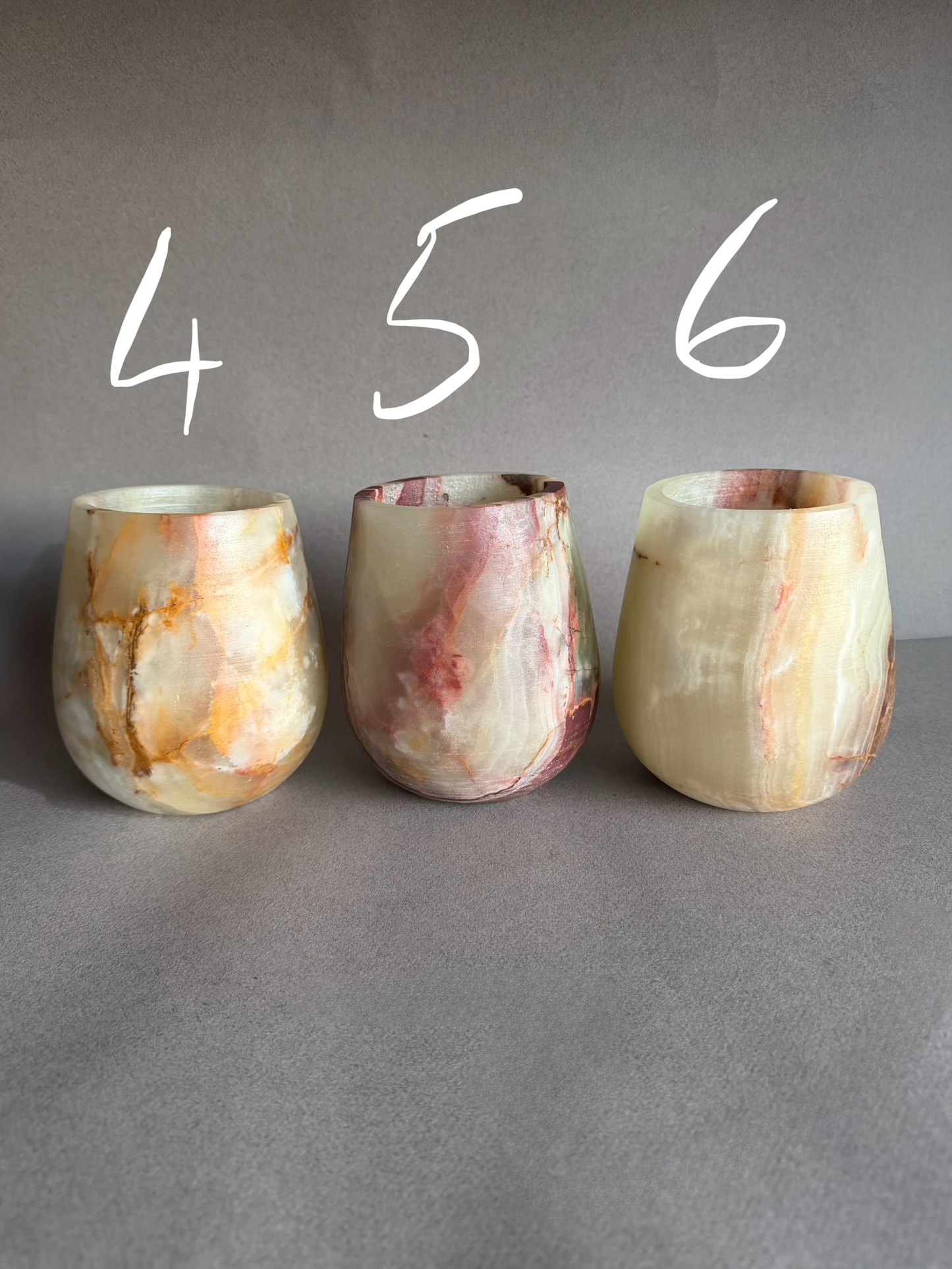 Three onyx cups with marbled patterns on a gray surface.