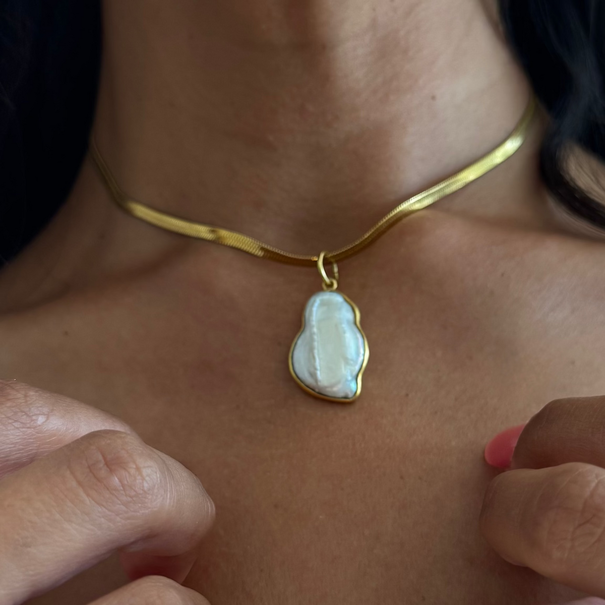 Close-up of a person wearing gold jewelry  with a pearl pendant including a necklace, earrings, and rings.