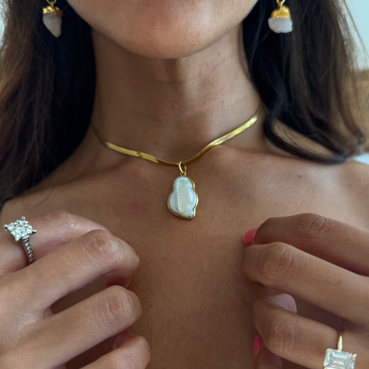 Close-up of a person wearing gold jewelry  with a pearl pendant including a necklace, earrings, and rings.