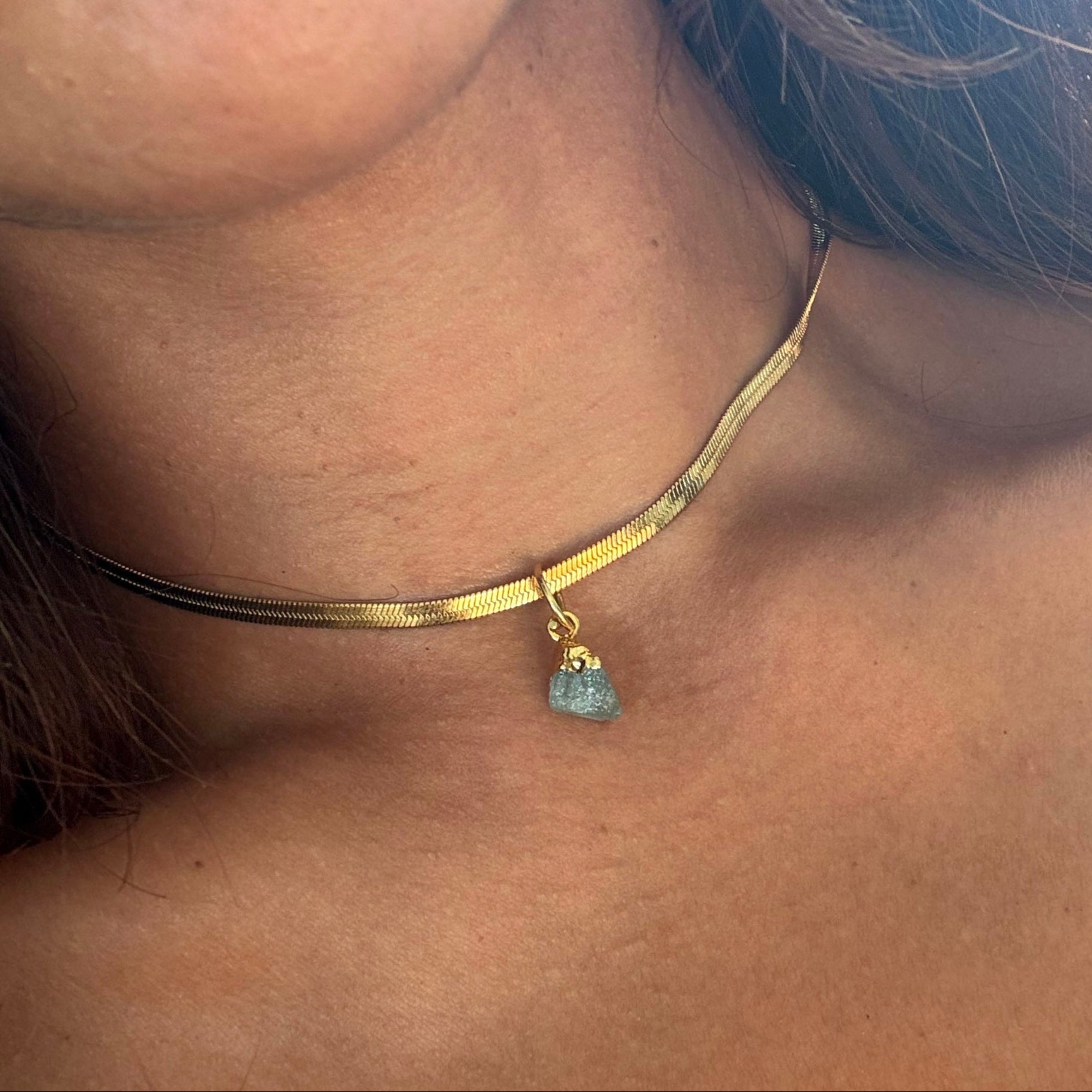 Gold choker necklace with a small aquamarine pendant worn by a person