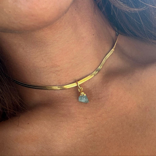 Gold choker necklace with a small aquamarine pendant worn by a person