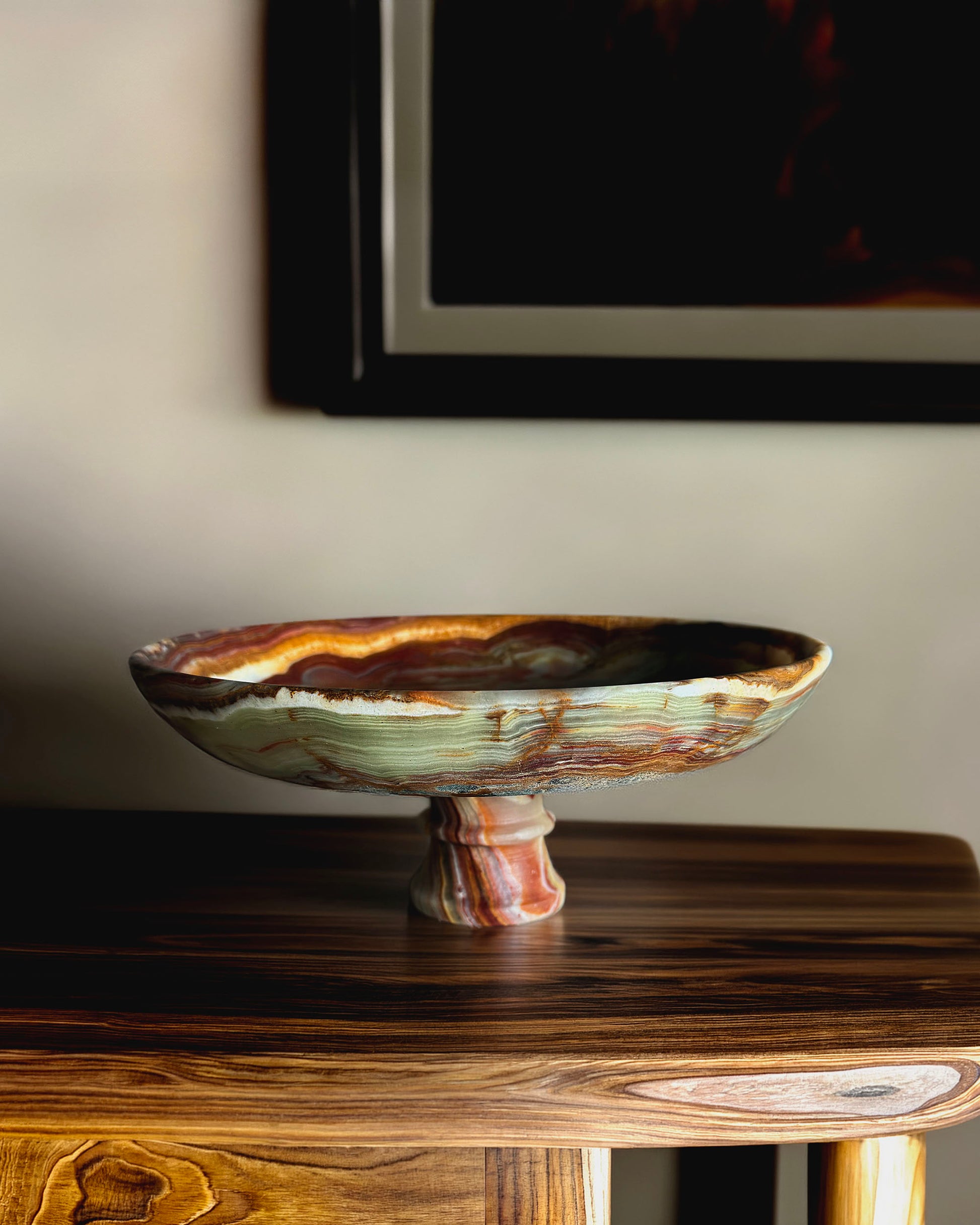 Decorative onyx pedestal bowl on a wooden surface with a blurred background
