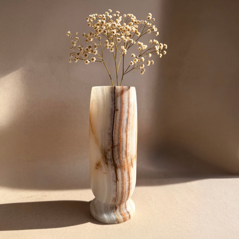 Hand-carved onyx Origin Vase in ivory and caramel with soft rust banding, lit against a pale neutral backdrop.
