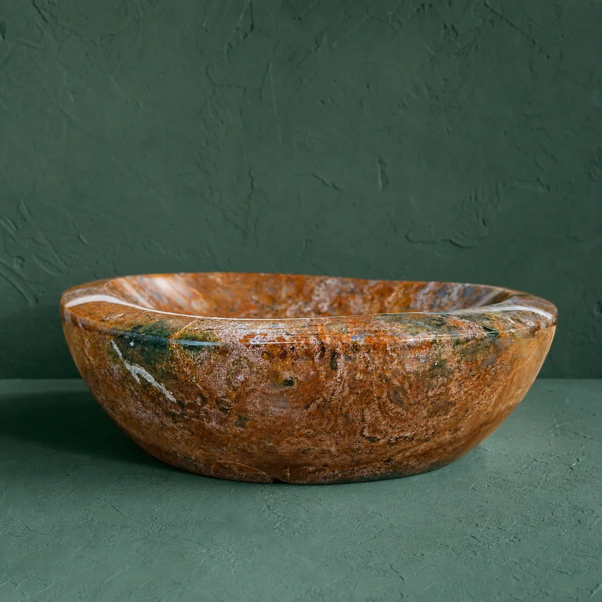 A round stone vessel sink bowl in a warm brown and orange marbled pattern with natural white and dark green veining, set against a dark green textured background.