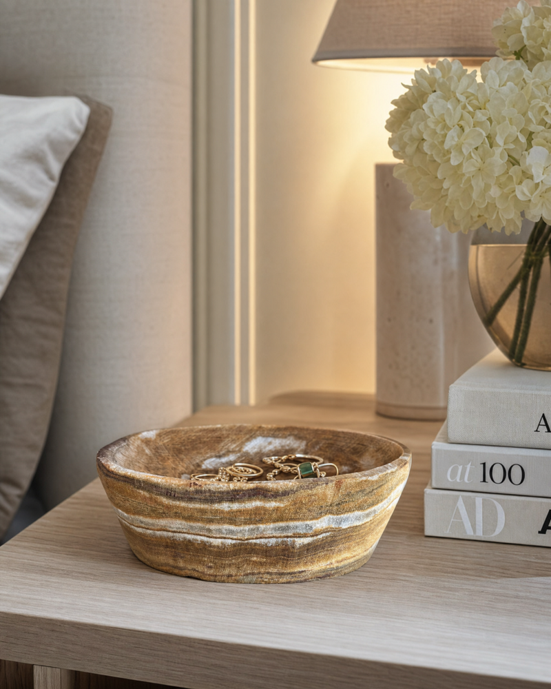 Natural onyx ring dish on bedroom nightstand holding gold rings and emerald jewelry — sculptural stone catchall by SAÉA.

