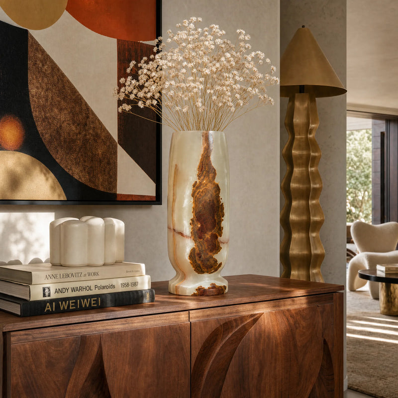 Decorative interior scene with a wooden cabinet, onyx vase with dried flowers, books, and abstract art.
