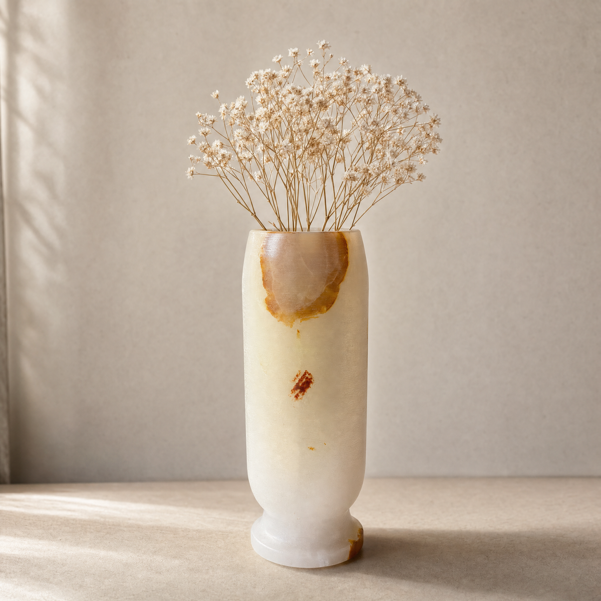 White onyx vase with a textured surface holding dried flowers on a neutral background