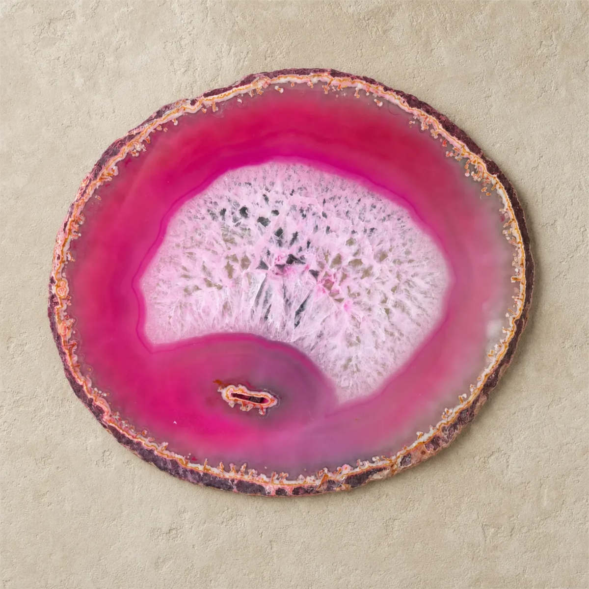 A circular agate slice wall decor piece with vibrant magenta pink and white crystalline patterns, displayed on a textured beige background.