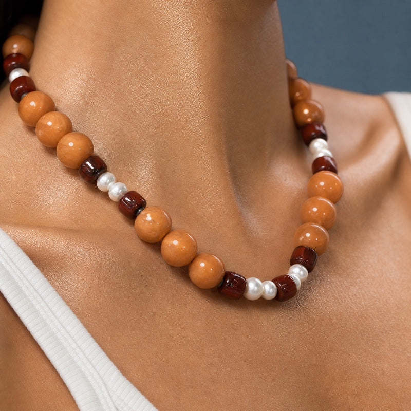 A close-up of a beaded necklace worn on a model's neck. The necklace features large, polished round beads in light tan, dark reddish-brown, and small white pearl-like accents.

Vintage carnelian, garnet and freshwater pearl beaded choker laid flat on wood, chunky caramel rounds with wine-red garnet and white pearls