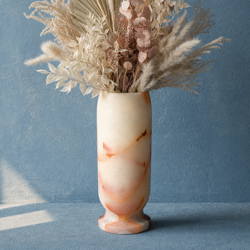 A decorative dried floral arrangement in a flared onyx vase, set against a textured blue wall and surface.