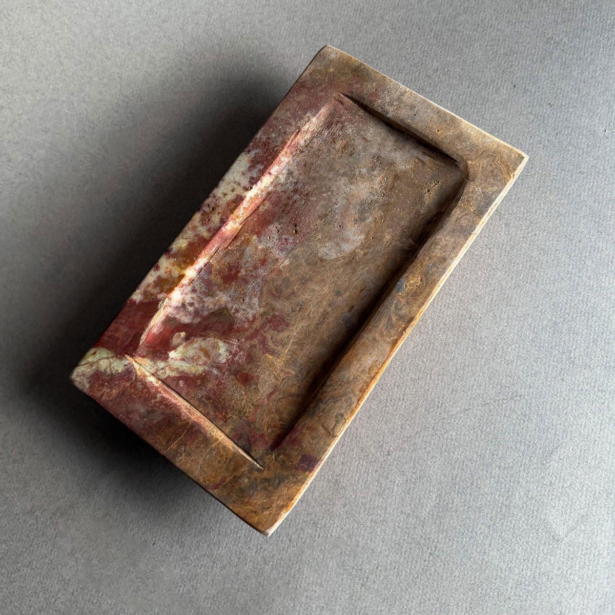 Hand-carved rustic onyx catchall tray in rust, amber, and honey tones with sculptural stepped-edge design on neutral gray backdrop

