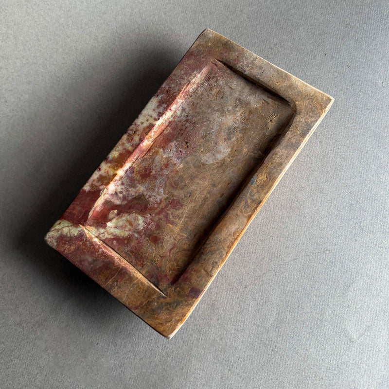 Hand-carved rustic onyx catchall tray in rust, amber, and honey tones with sculptural stepped-edge design on neutral gray backdrop

