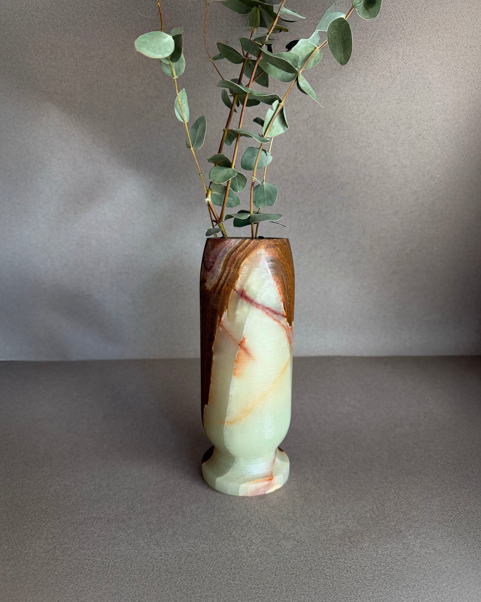 Decorative vase with a natural stone pattern containing greenery on a gray background