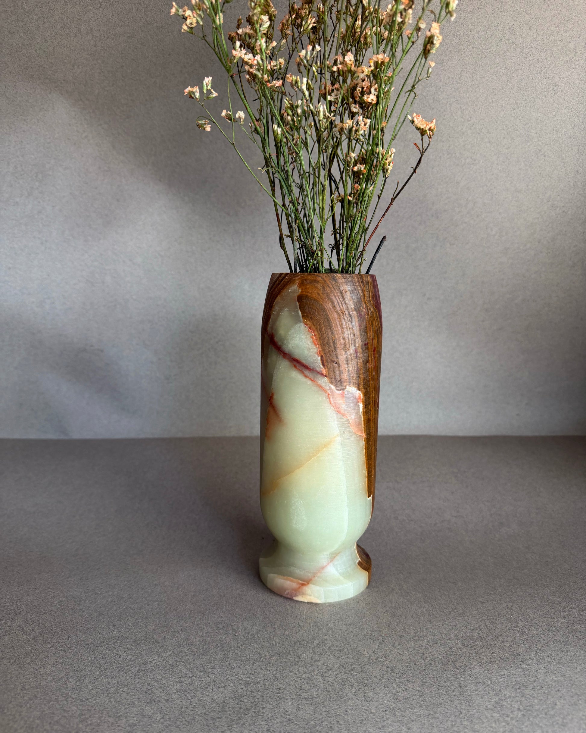 Decorative onyx alabaster stone vase with marbled design and dried flowers on a gray backgrounds