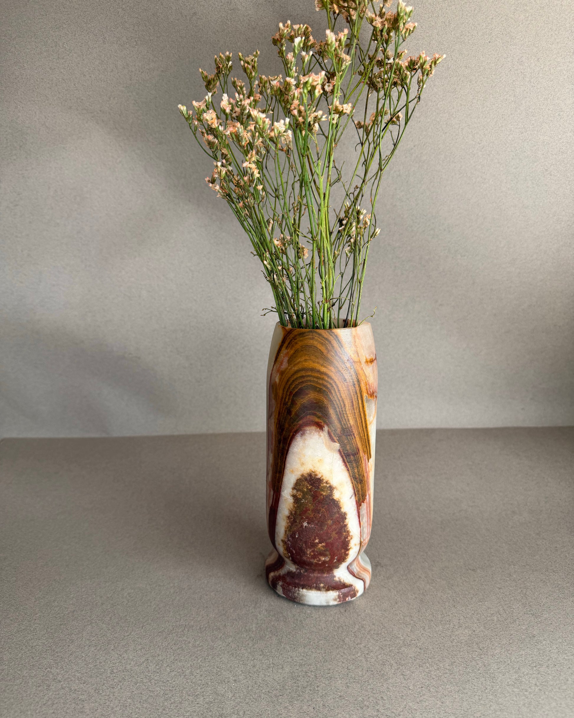 Decorative vase with a natural stone pattern containing dried flowers on a neutral background