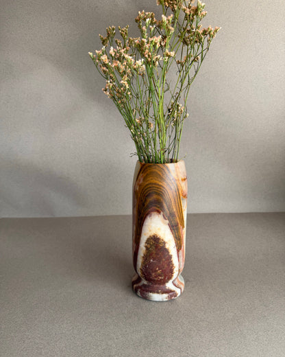 Decorative vase with a natural stone pattern containing dried flowers on a neutral background