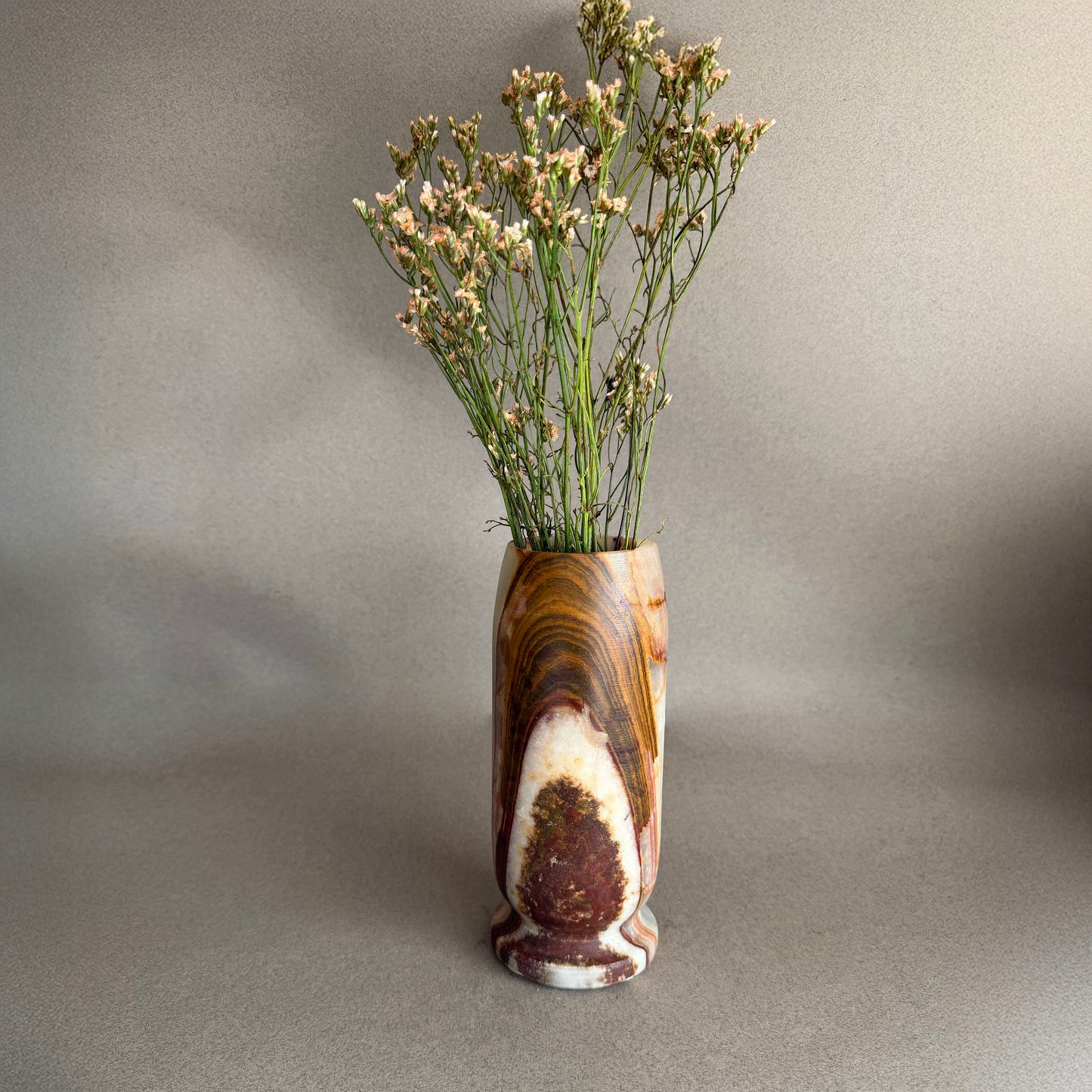 Decorative vase with a natural pattern containing dried plants on a plain background
