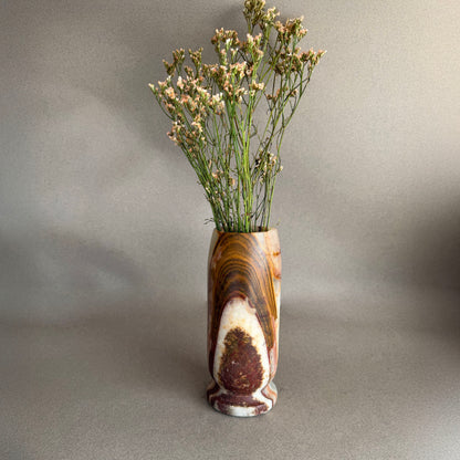 Decorative vase with a natural pattern containing dried plants on a plain background