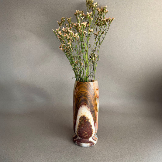 Decorative vase with a natural pattern containing dried plants on a plain background