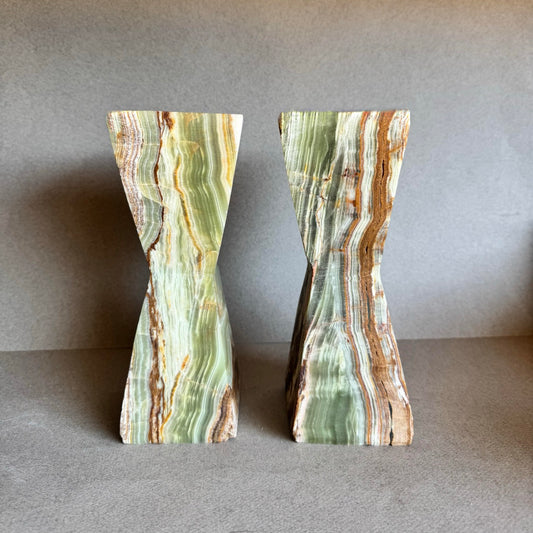 Pair of green onyx hourglass candle holders with sage, honey, and clay veining on grey backdrop

