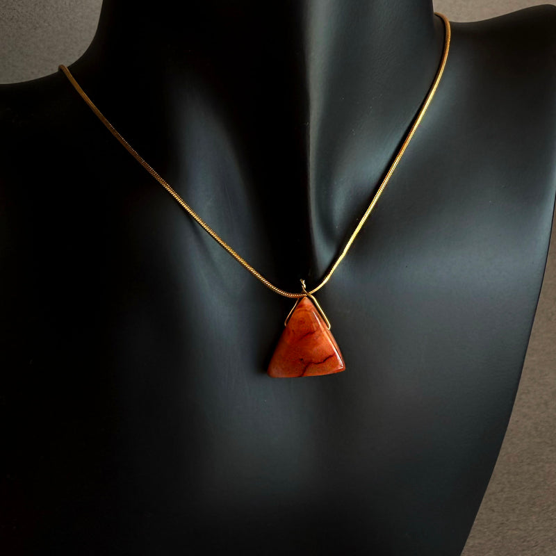 Necklace with a triangle-shaped pendant on a mannequin Carnelian triangle pendant necklace on gold filled snake chain worn on black sculptural bust
