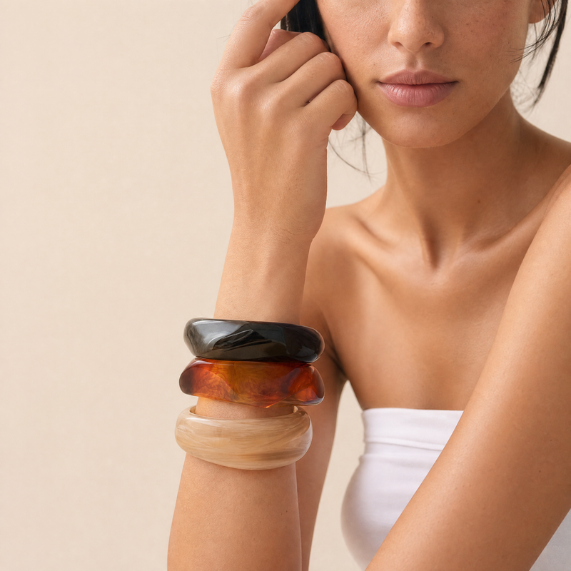 Woman wearing a stack of three cylindrical bracelets on her wrist against a beige background

Chunky marbled resin stacking bangles in espresso, amber, and alabaster stacked on a model's wrist
