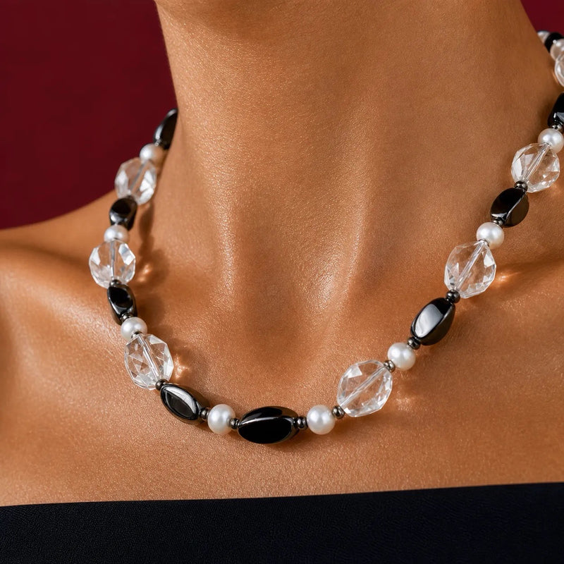 A close-up of a beaded necklace worn on a mannequin or display bust. The necklace features faceted clear beads, glossy black oval beads, and small white pearl-like beads separated by dark metallic spacers, set against a dark red background.

 Close view of a vintage necklace with faceted clear rock crystal quartz, black onyx, twisted hematite and freshwater pearls
