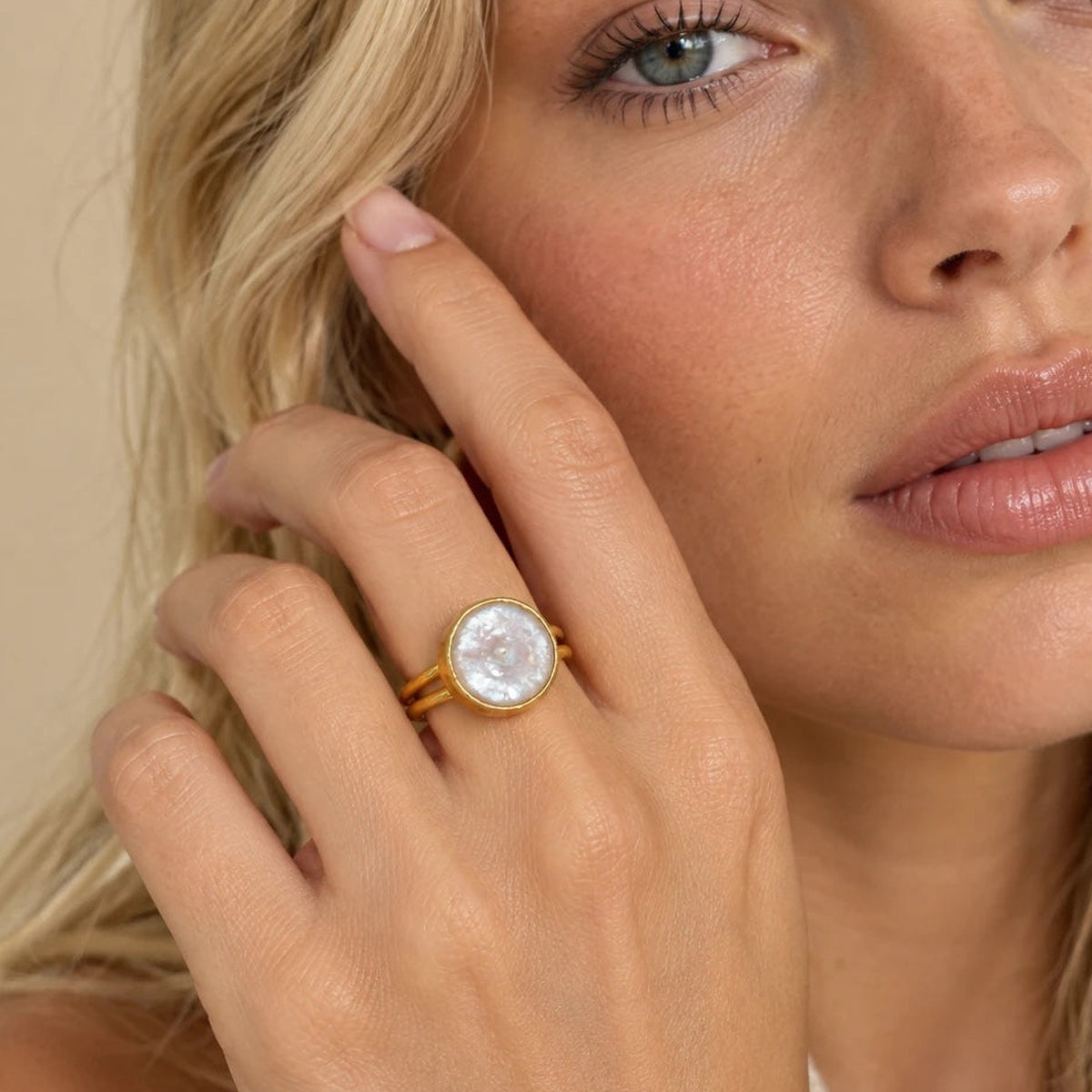Freshwater coin pearl ring worn on a hand raised to the cheek, the round white pearl in a hammered 22k gold-filled bezel